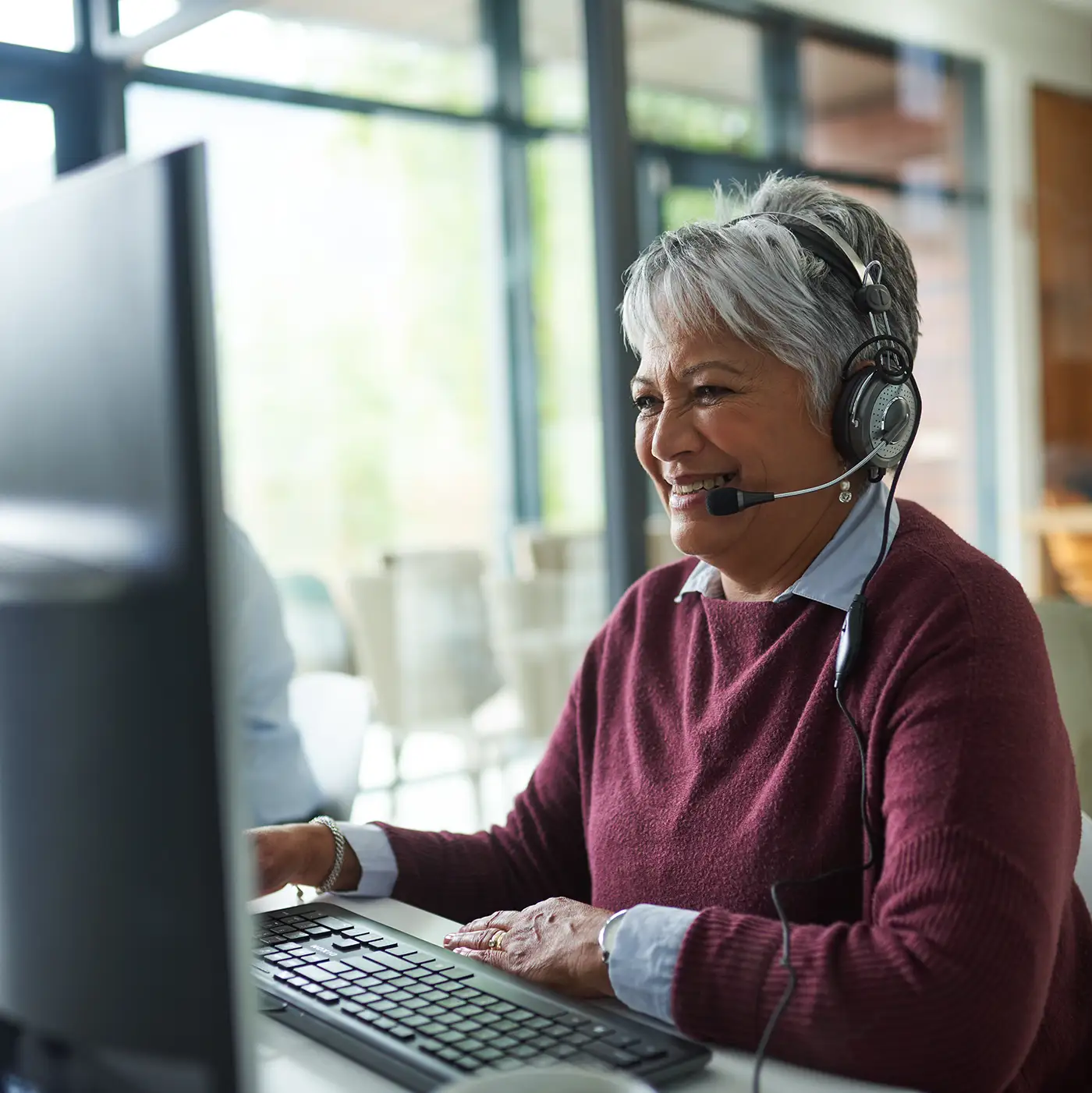 A woman in front of a computer monitor answering a phone in business setting
