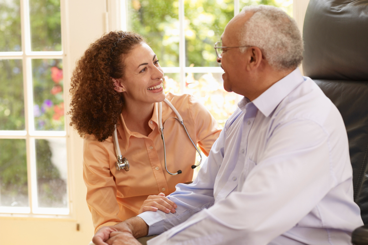 Woman caretaker kneeling next to senior man in chair