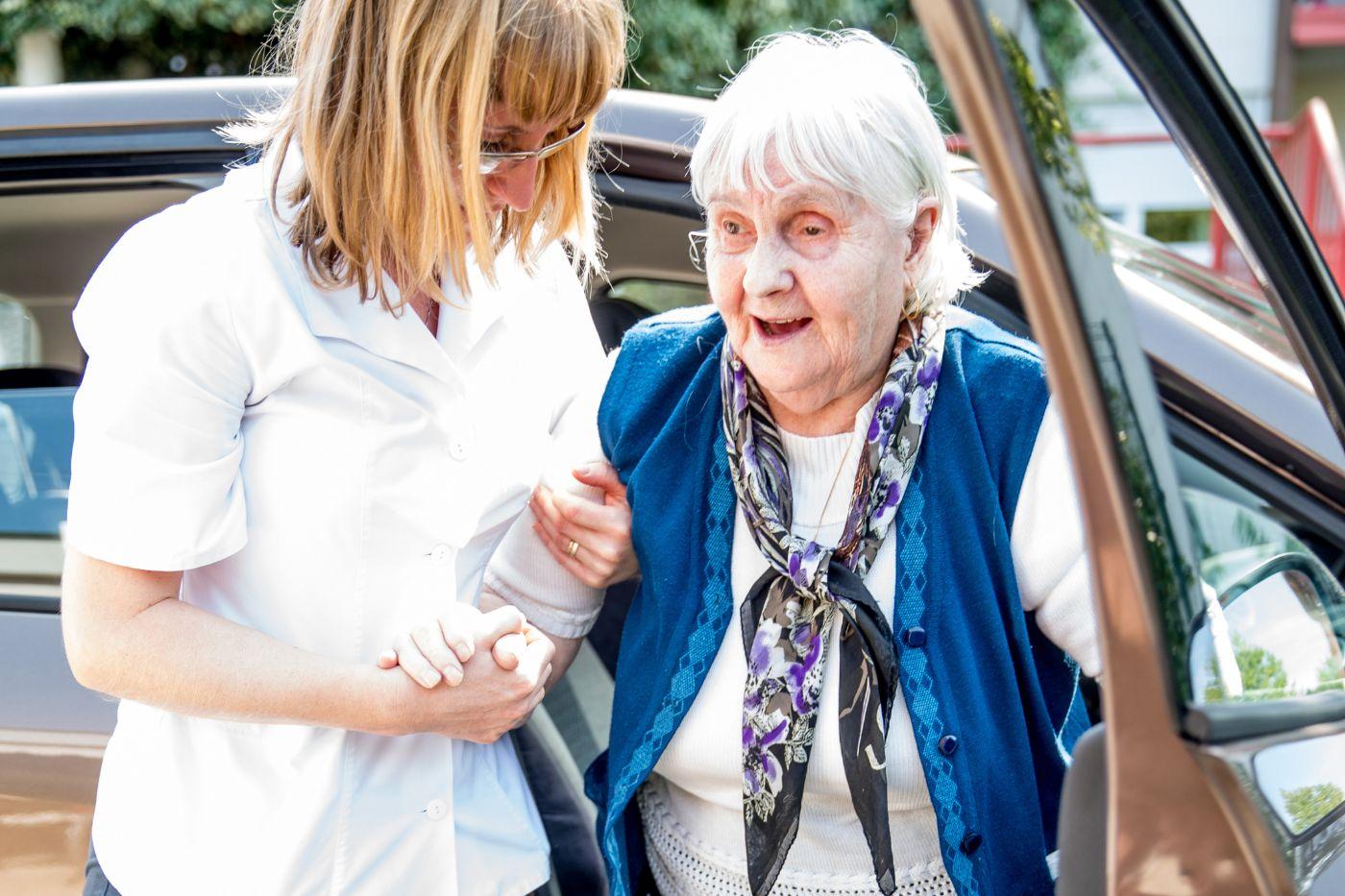 Woman helping senior woman out of car